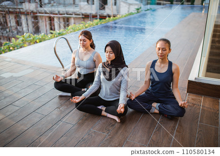 three young woman in lotus pose meditating and relaxing near swimming pool 110580134