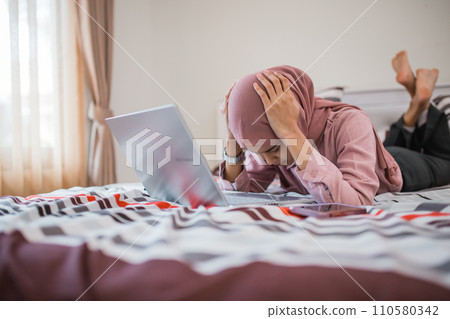 Muslim woman gets dizzy when using laptop while lying on the bed 110580342