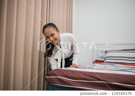 housemaid woman smiles while putting up bed sheets in room housemaid woman smiles while putting up bed sheets in room 110580376