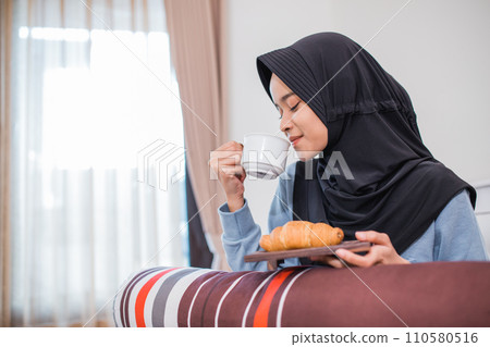 veiled woman drinking a cup of tea and bread on the bed veiled woman drinking a cup of tea and bread on the bed 110580516