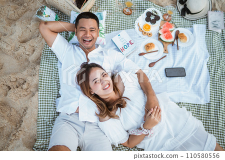 wife takes cell phone call while sitting with husband on blanket picnicking wife takes cell phone call while sitting with husband on blanket picnicking 110580556