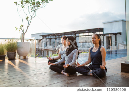 three young woman sitting near swimming pool in lotus position at resort three young woman sitting near swimming pool in lotus position at resort 110580606