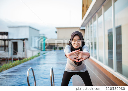 Smiling Muslim woman stretching her arms before meditation near the swimming pool 110580980