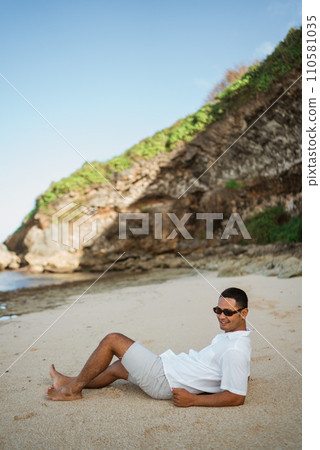 young Asian man with sunglasses lying on a tropical beach 110581035