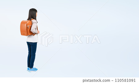 Rear view of a female elementary school student standing with a school bag on her back 110581091