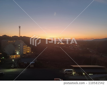 日落景色，左邊山上有一座鋼塔，下面是停車場、鐵軌和房屋，遠處是海洋。 110581542