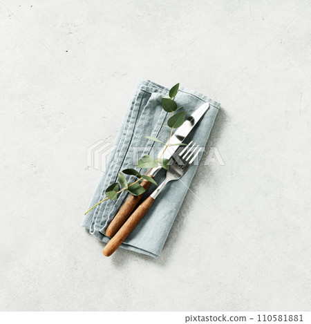 Table setting with linen napkin, fork, knife and eucalyptus on grey background Table setting with linen napkin, fork, knife and eucalyptus on grey background 110581881