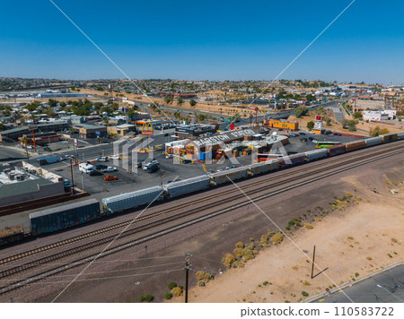 Aerial view of Barstow, a quaint suburb along Route 66, featuring the Barstow Station, parallel railroad tracks, a freight train, and a clear, sunny desert landscape. 110583722