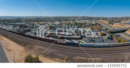 Aerial view of Barstow, California, showcasing the Barstow Station, diverse architecture, and scenic mountain backdrop along historic Route 66 under a clear, sunny sky. 110583731