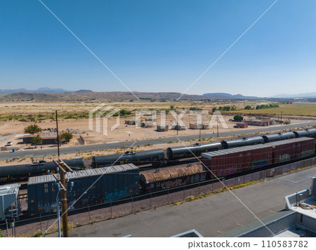 Captivating semi-arid landscape featuring a freight train with cargo containers and tankers, sparse desert vegetation, distant mountains, and clear blue skies, perfect for transportation themes. 110583782