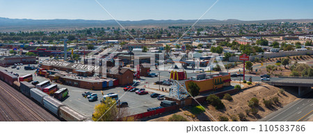 Aerial view of Barstow, California, showcasing a sunny desert landscape with diverse architecture, busy roads, green spaces, and a mountainous horizon, highlighting local commerce and transportation. 110583786