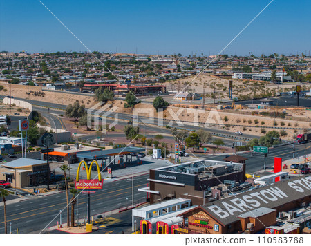 Elevated view of Barstow, California, capturing the bustling urban landscape, commercial brands, and traffic on Route 66, set against a backdrop of gentle hills and clear skies. 110583788