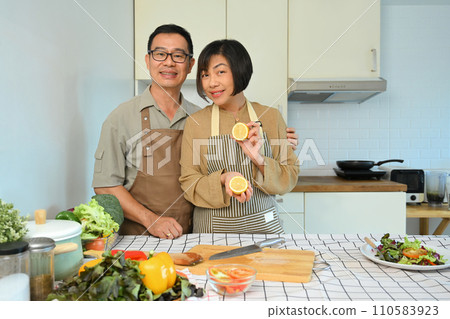 Happy retired couple in aprons cooking healthy food with organic ingredients in kitchen. Healthy lifestyle concept. 110583923