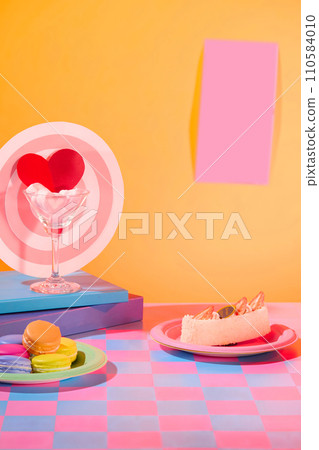 Background with pastel colors. Marshmallow inside a cocktail glass, macarons and cakes on a plate. A piece of paper is stuck on the orange wall. Empty space for text design. Background with pastel colors. Marshmallow inside a cocktail glass, macarons and cakes on a plate. A piece of paper is stuck on the orange wall. Empty space for text design. 110584010