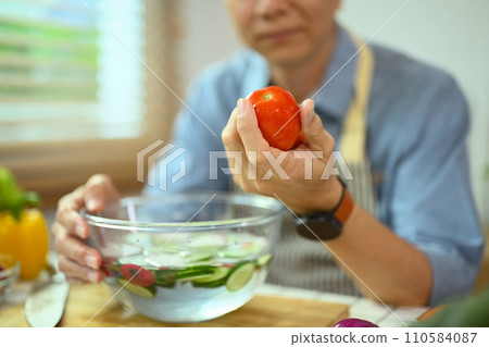 Select on senior man hand holding fresh tomato, preparing healthy salad in kitchen Select on senior man hand holding fresh tomato, preparing healthy salad in kitchen 110584087