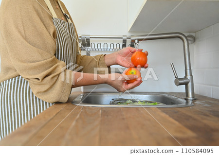 Cropped shot senior housewife in apron washing fresh vegetables for salad in kitchen Cropped shot senior housewife in apron washing fresh vegetables for salad in kitchen 110584095