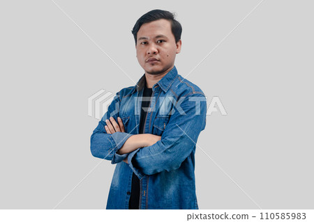 Young Asian Man folded arms looking at camera with bad face expression Young Asian Man folded arms looking at camera with bad face expression 110585983