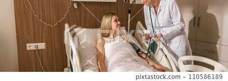Doctor checking blood pressure of young woman patient in ward of modern clinic Doctor checking blood pressure of young woman patient in ward of modern clinic 110586189