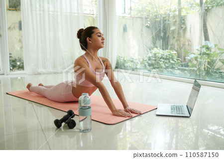 Young woman following video on laptop screen when working out at home in the morning 110587150