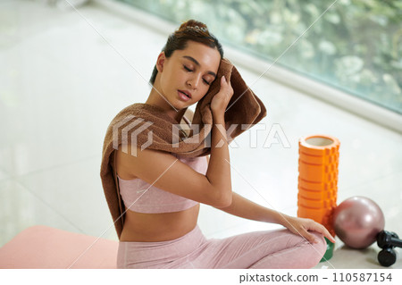 Tired young woman wiping off sweat after intense workout 110587154
