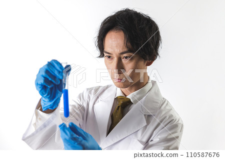 A man in a white coat looking into a test tube 110587676