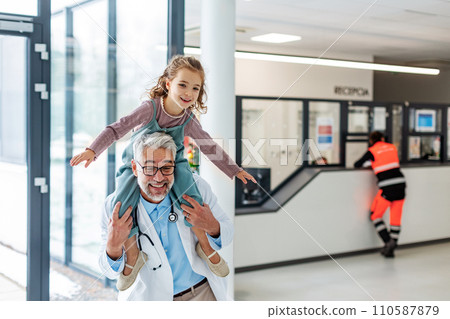 Portrait of a pediatrician with a little patient sitting on his shoulders, piggyback. Friendly relationship between the doctor and the child patient. Portrait of a pediatrician with a little patient sitting on his shoulders, piggyback. Friendly relationship between the doctor and the child patient. 110587879