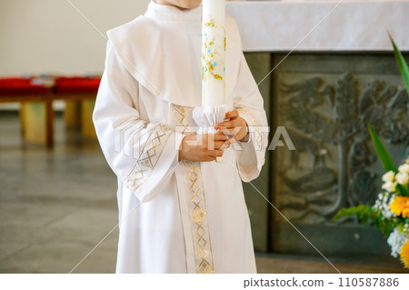 Little kid boy receiving his first holy communion. Happy child holding Christening candle. Tradition in catholic curch. Kid in a white traditional gown in a church near altar. Little kid boy receiving his first holy communion. Happy child holding Christening candle. Tradition in catholic curch. Kid in a white traditional gown in a church near altar. 110587886