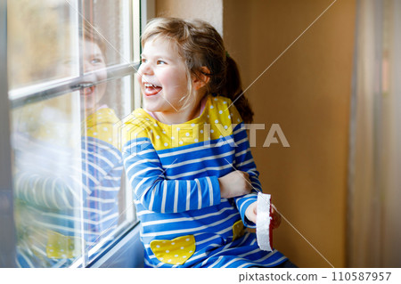 Cute little girl by window holding selfmade heart as gift for Valentine's day, Mother's day or birthday. Adorable happy smiling child indoors. 110587957