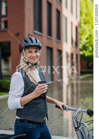 Beautiful middle-aged woman commuting through the city, buying, drinking coffe in front of office. Female city commuter traveling from work by bike after a long workday. Beautiful middle-aged woman commuting through the city, buying, drinking coffe in front of office. Female city commuter traveling from work by bike after a long workday. 110588069