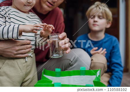 Father teaching son recycle waste. Boy sorting the waste according to material into colored bags. 110588102