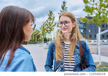 Teenage talking smiling girl looking at woman, outdoor 110588229