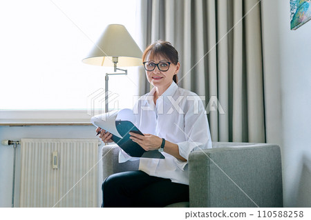 Portrait of middle-aged woman with clipboard sitting in an office chair 110588258