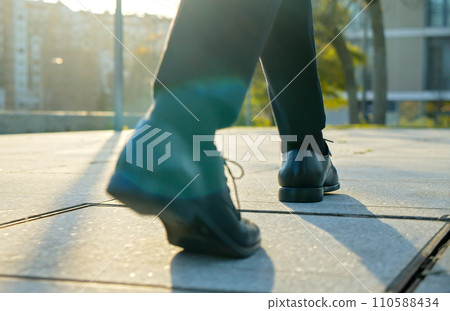 Legs of a businessman in fashionable shoes walking outdoors. Business concept. Close-up view to the businessman in a black new shoes walks on the street. Stylish men wears. Low angle. Rear view. 110588434
