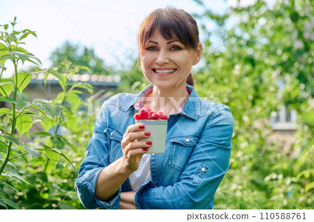 Happy woman in raspberry bushes garden, with cup ripe raspberries 110588761
