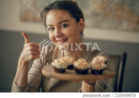 A young woman shows a cool sign with cupcakes in her hand. cream decoration. The bakery chef bakes cakes in the kitchen A young woman shows a cool sign with cupcakes in her hand. cream decoration. The bakery chef bakes cakes in the kitchen 110589078