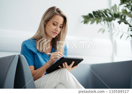 Portrait of female doctor sitting in office, looking at test results CT scans in tablet. Female surgeon in modern medical clinic. 110589527
