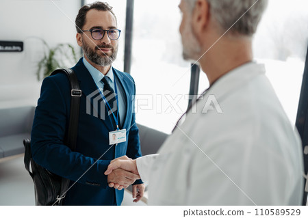 Pharmaceutical sales representative shaking hands with doctor in medical building. Doctor greeting hospital director, manager in private clinic. 110589529