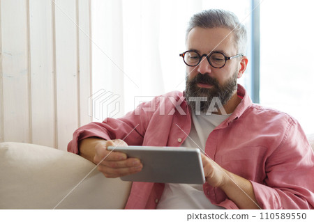 Man using smart thermostat, adjusting, lowering heating temperature at home. Man watching tv show on tablet, video streaming services with movies and tv shows. Man using smart thermostat, adjusting, lowering heating temperature at home. Man watching tv show on tablet, video streaming services with movies and tv shows. 110589550
