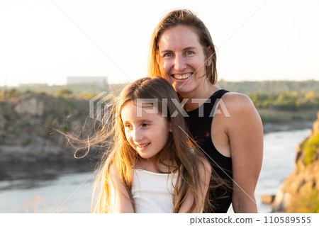 Happy mom and daughter relaxing on rocks in nature against the backdrop of the river. Happy Motherhood, Mother's Day 110589555