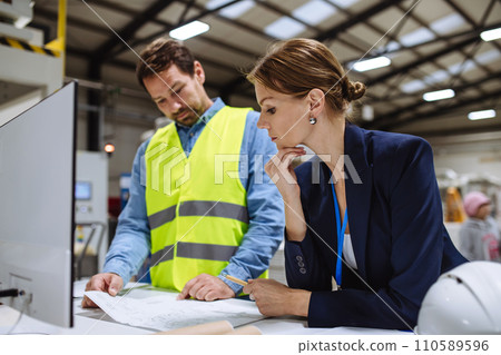 Female warehouse director talking with production manager, discussing new order, preparing products for shipment, delivery, checking stock in warehouse. 110589596