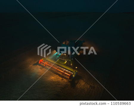 Aerial view of a tractor and harvester working in a field during night. Agriculture and cultivation of industrial farms. Agribusiness. Aerial view of a tractor and harvester working in a field during night. Agriculture and cultivation of industrial farms. Agribusiness. 110589663