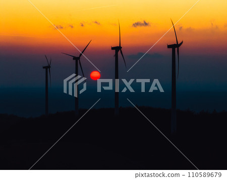 Aerial landscape photography of sunrise over nature with wind turbines. Windmill in soft morning light with forest, trees around. Concept of wind power as clean, renewable energy source. 110589679