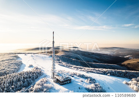 Aerial view of transmitter, cell tower surrounded by a forest during winter. Drone view of snowy landscape, christmas holidays. 110589680
