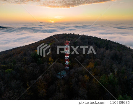 Aerial view of transmitter, cell tower surrounded by a forest and clouds, mist. 110589685