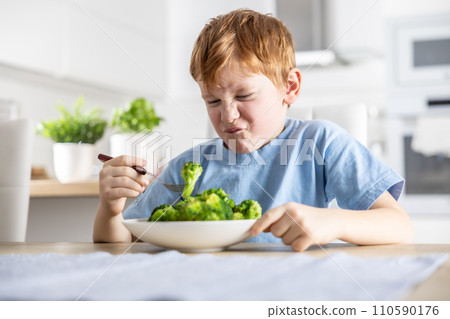 The little boy looks with distaste at the broccoli on his fork 110590176