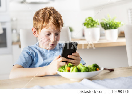 View of smart cute boy using smartphone before lunch in kitchen at home 110590186