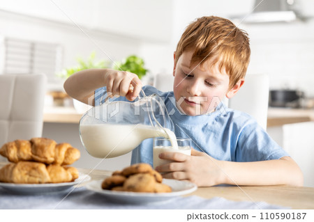 A little boy pours himself fresh milk during breakfast A little boy pours himself fresh milk during breakfast 110590187