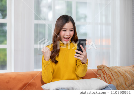 Millennial asian young woman looking mobile phone laughing with good news or discount voucher for shopping online at home.Happy and cheerful woman looking on cellphone app read message feel excited Millennial asian young woman looking mobile phone laughing with good news or discount voucher for shopping online at home.Happy and cheerful woman looking on cellphone app read message feel excited 110590991