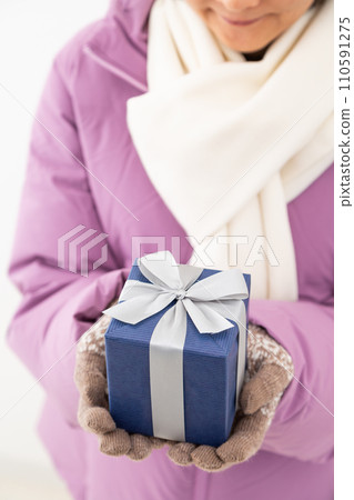 Middle-aged woman in winter clothes holding a present 110591275