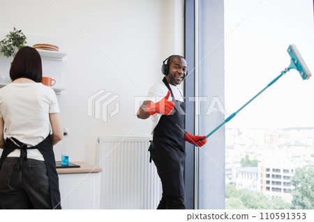 African washing windows with mop, listening to music in headphones and dancing. 110591353